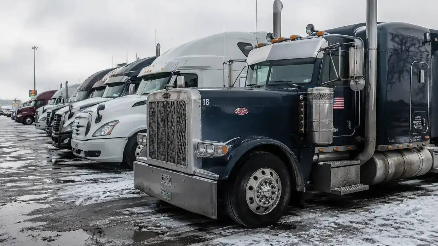 Truck stop parking lot in winter, snow on the ground, Peterbilt parked with flag still mounted and intact