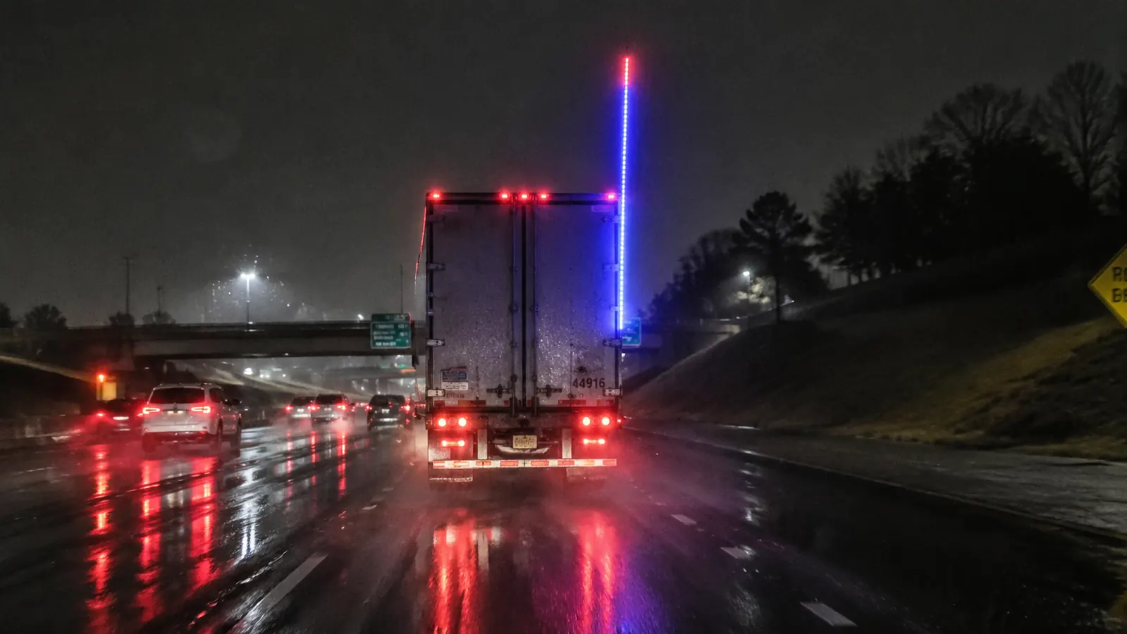 Rainy night highway scene with semi truck running LED whip light visible through rain