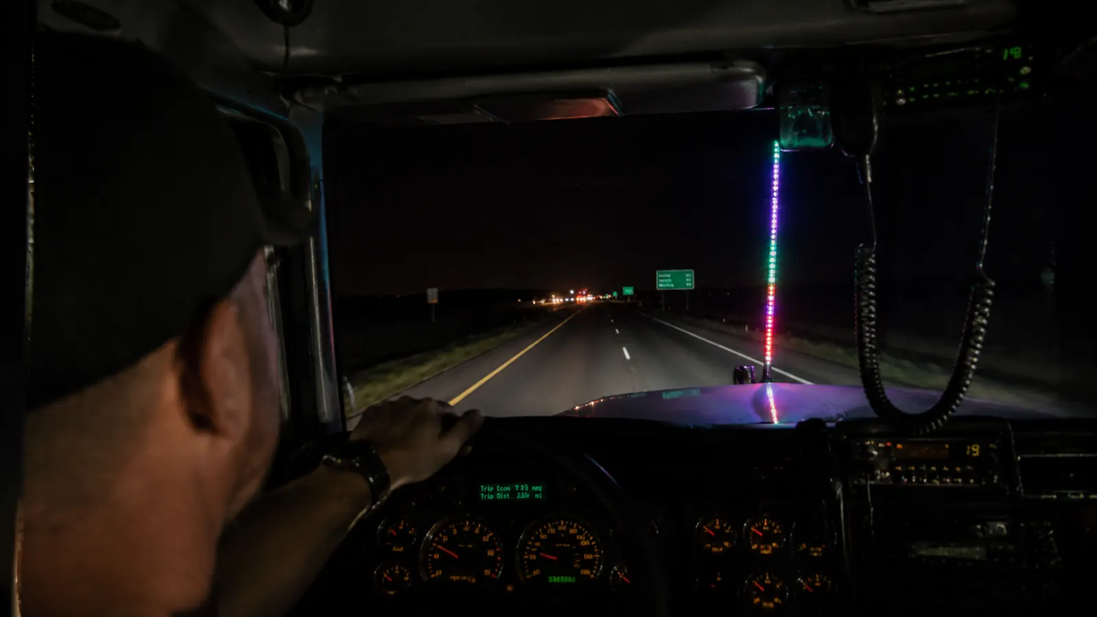 Night view from inside a truck cab looking forward through windshield, faint LED glow from the mounted whip pole reflected on the hood, Kansas highway dark ahead
